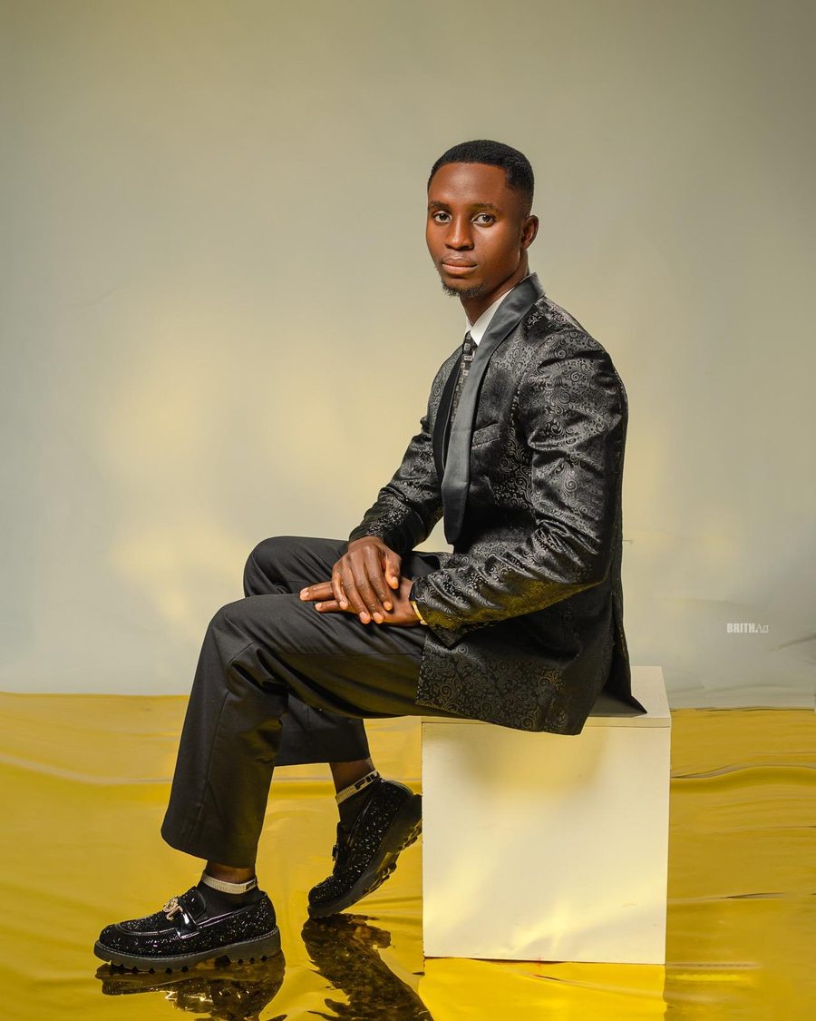 Joshua Gboga seated on a white block against a gold backdrop